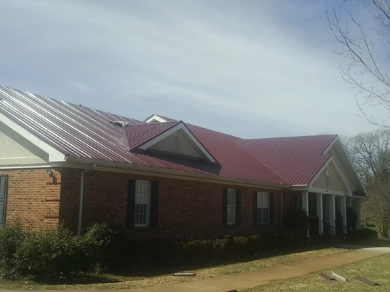 Red metal roof with gabled entries on a long brick building, from a Hail Damage Roof Repair job in New Smyrna Beach