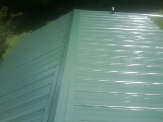 New green metal panels meeting at the ridge of a roof — Flat Roof Repair work by our crew in New Smyrna Beach