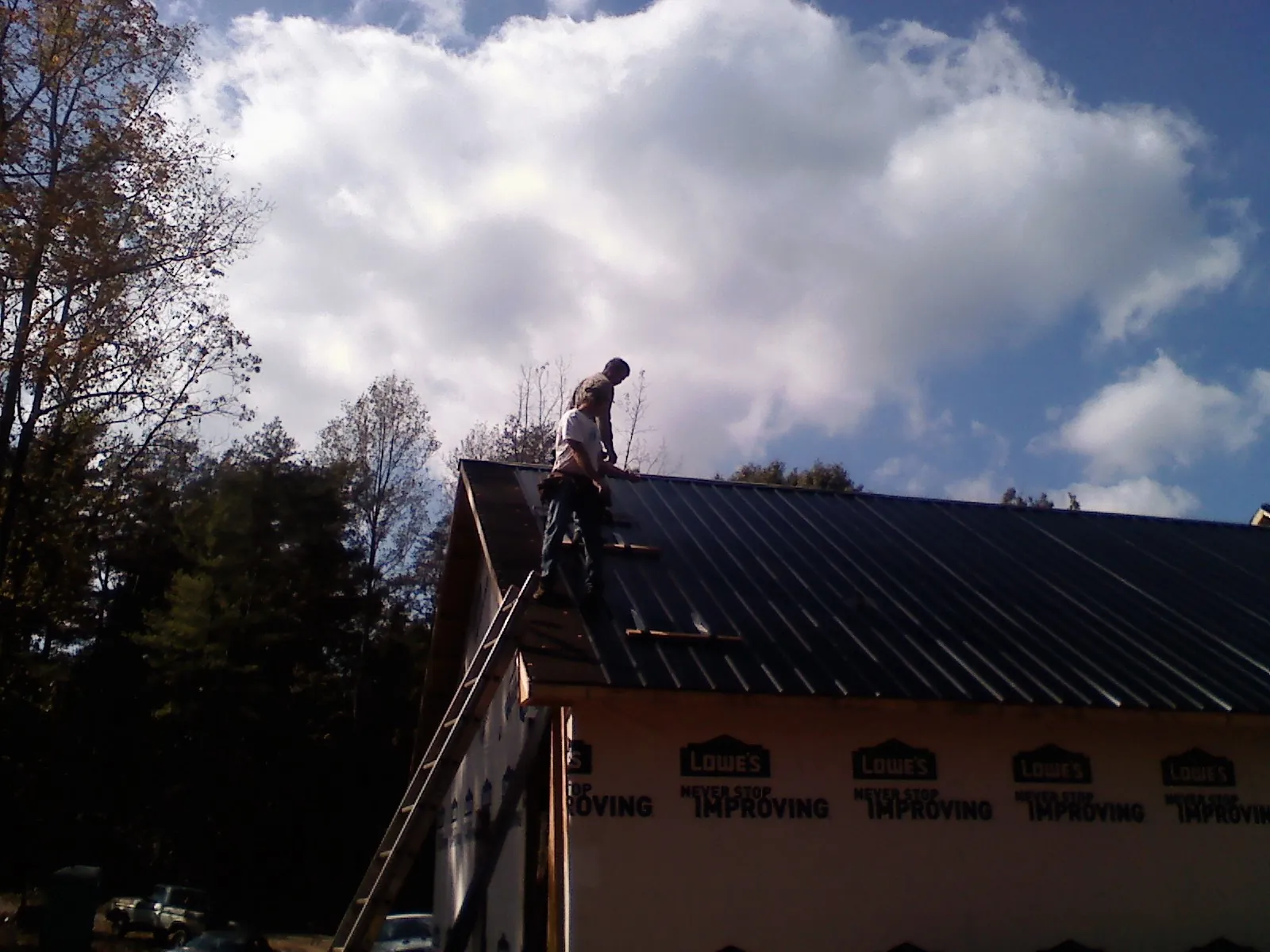 Roofer fastening dark metal panels high against a cloudy sky, from a Roof Inspection job in New Smyrna Beach
