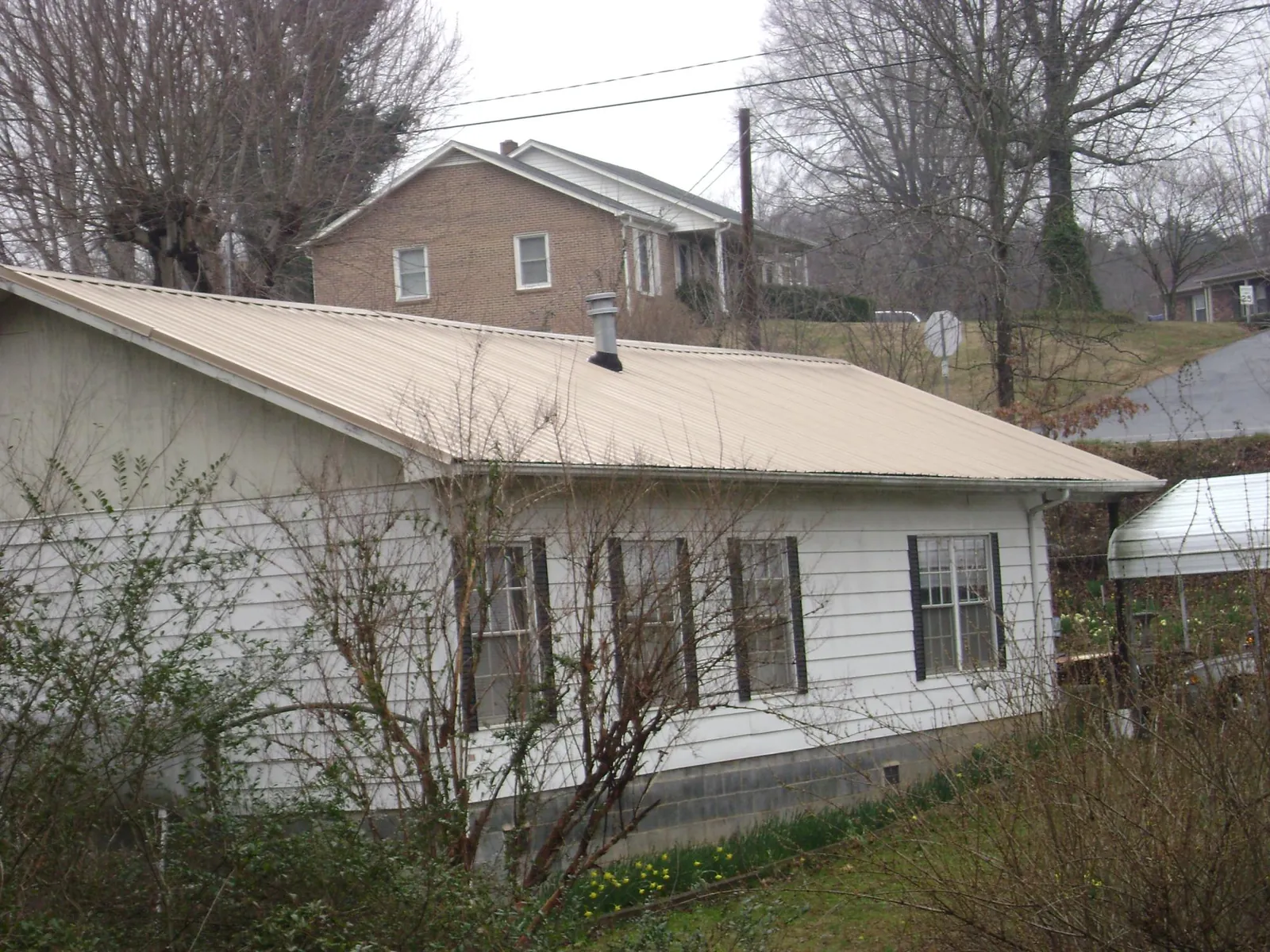 Tan metal roof on a white sided house set into a hillside — Commercial Roofing by Roofing Brothers in New Smyrna Beach
