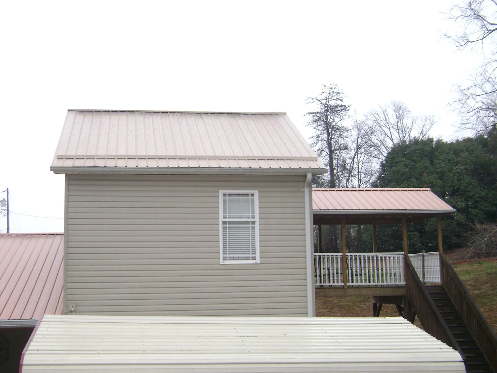 Tan metal roofs on a two story addition and attached porch, from a Roof Replacement job in New Smyrna Beach